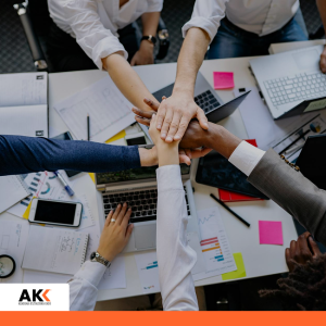 Zespół pracowników łączy dłonie nad stołem z dokumentami i laptopami – szkolenie Profesjonalna obsługa pacjenta w rejestracji medycznej