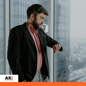 Mężczyzna w marynarce sprawdza godzinę na zegarku stojąc przy oknie z widokiem na miasto – szkolenie AI w biznesie i przemyśle od użycia do strategii