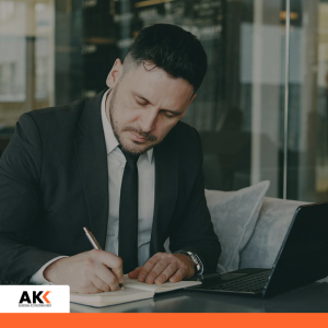 Mężczyzna w garniturze podpisujący dokumenty przy laptopie, symbolizujący formalne aspekty zatrudnienia.