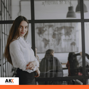 Kobieta stojąca w biurze na tle zespołu, symbolizująca zarządzanie kadrami i płacami.