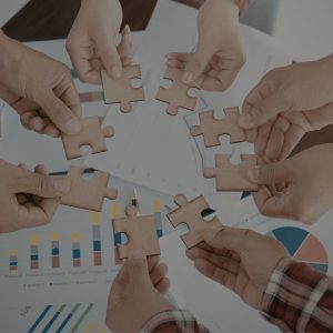 Dłonie trzymające pasujące do siebie puzzle na tle wykresów – warsztaty z umiejętności miękkich w Akademii Kształcenia Kadr.